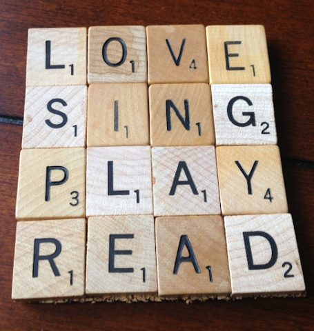 A coaster made out of wooden Scrabble pieces. Spelling out the words: "Love", "Sing", "Play", and "Read".