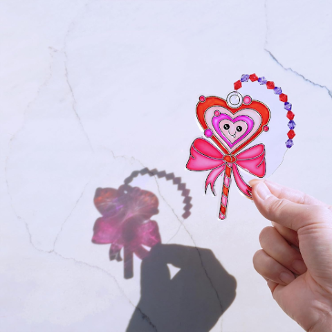 A Valentine's Day themed suncatcher being held by a hand against a white backdrop. 