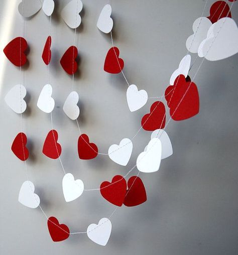 Strung up red and white paper hearts against a gray wall. 